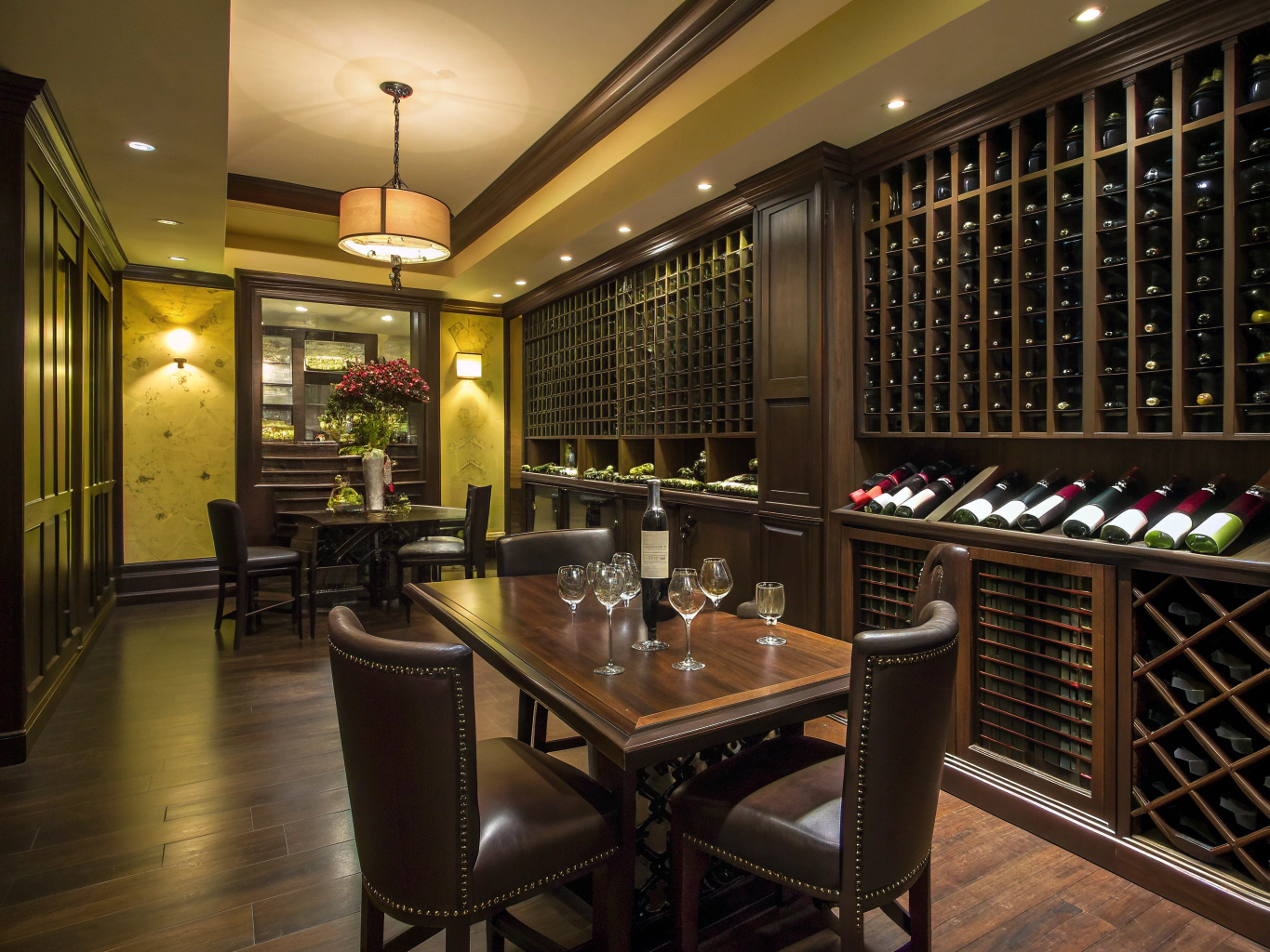 Glass-enclosed climate-controlled wine room with warm lighting, brick accent wall, and tasting lounge seating
